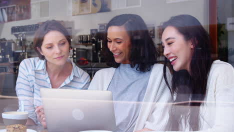 Amigas-Mirando-Una-Computadora-Portátil-Juntas-En-Una-Cafetería