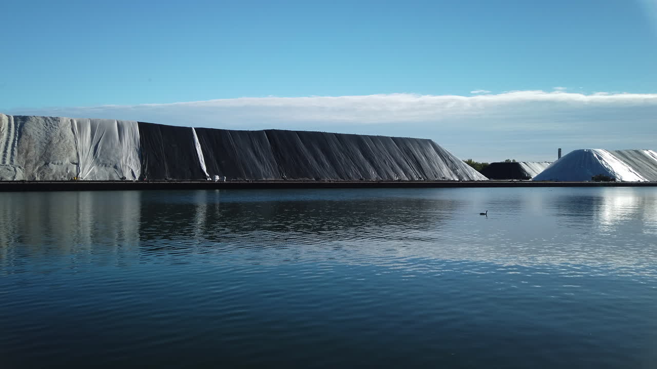 Tonnes of white salt, stored under black tarps in Toronto's inner harbor, wide shot panning left to right