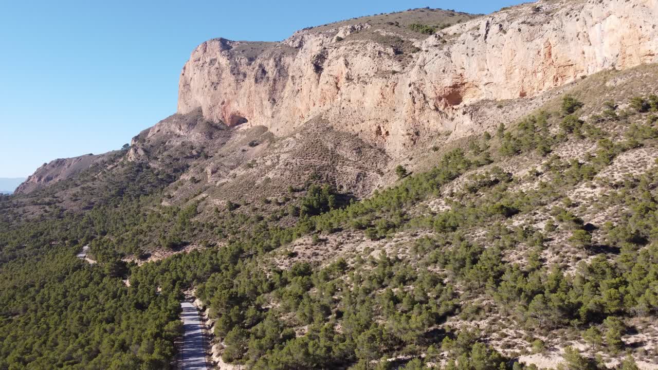 disparo de un avión no tripulado de una montaña en un día soleado, también mostrando una carretera y árboles