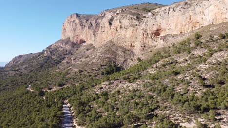 Toma-De-Drone-De-Una-Montaña-En-Un-Día-Soleado,-Que-También-Muestra-Una-Carretera-Y-árboles.