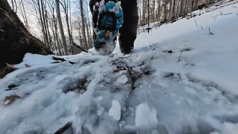 Close-up-shot-of-a-person-walking-on-a-snowy-mountain-path-in-a-forest-with-boots-with-hiking-ice-spikes