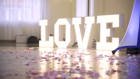 a young couple dancing in front of huge lighting love sign with lots of flowers on the floor