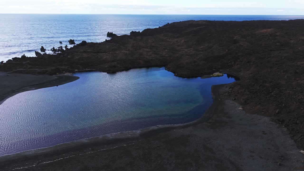Veduta aerea del Lago Verde a Lanzarote, Isole Canarie, con acqua blu, roccia vulcanica nera e cielo nuvoloso, ideale per concetti di viaggio e turismo.
