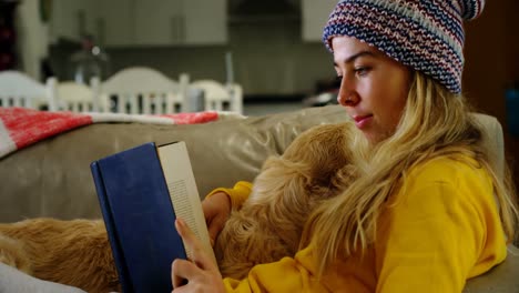 Woman-reading-book-with-her-dog-on-sofa-at-home-4k