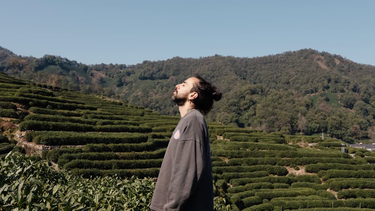 A man stands in profile among Longjing tea terraces in Hangzhou, Zhejiang, China