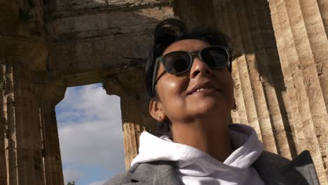 Mujer-Con-Gafas-De-Sol-Sonriendo-A-La-Vida-Visitando-Un-Templo-Griego-Durante-Un-Día-Soleado