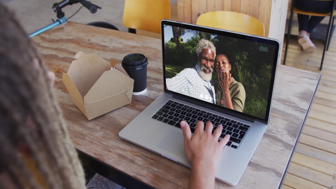 mujer tomando un bocadillo mientras hace una videollamada en una computadora portátil en una cafetería