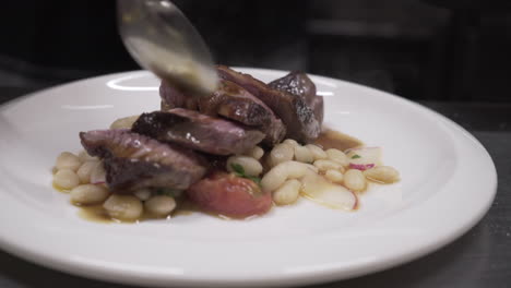 chef pouring sauce over sliced beef and beans with radishes