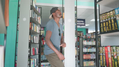 happy student wearing casual t shirt and backward cap dancing playfully between rows of bookshelves in bright library interior filled with colorful books and modern study atmosphere
