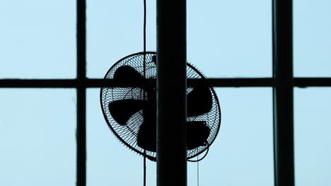 silhouette of a ceiling fan against windows