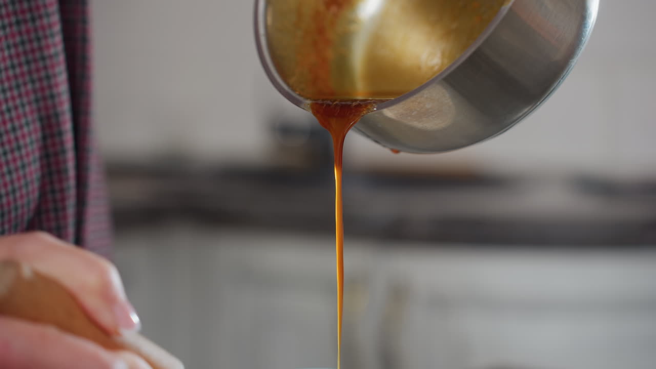 Close-up of person in plaid clothing pouring rich red soup from stainless pot into white bowl while stirring, warm liquid flows smoothly as cook prepares homemade meal in modern kitchen