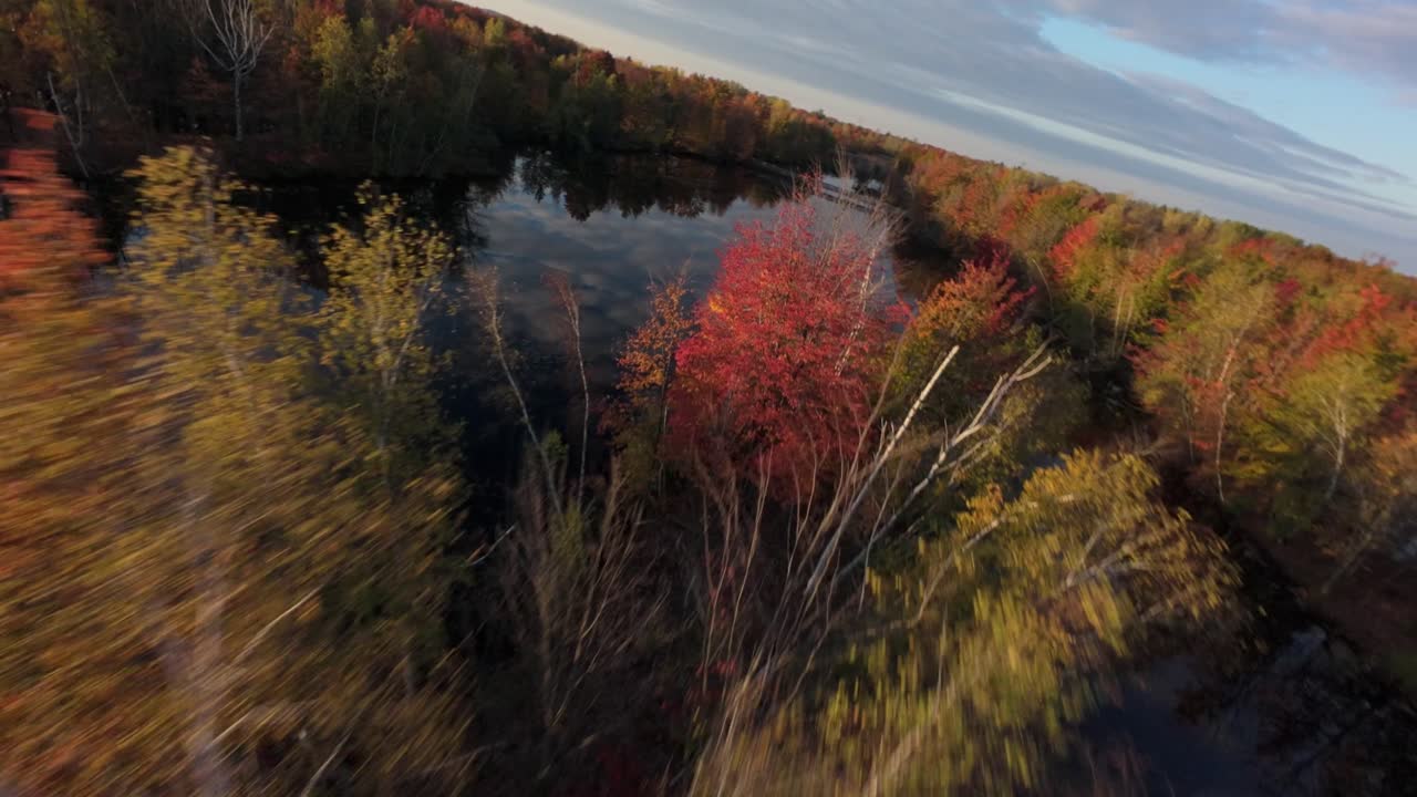 FPV drone flight gliding through aerial view to close to lake colourful fall foliage and reflective water channels at dusk in Sainte-Julie, Québec, Canada