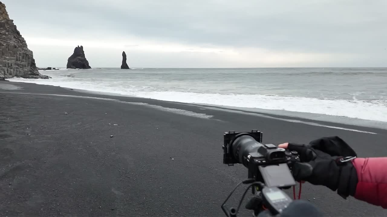 A video of Iceland's black sand beach shows dramatic waves crashing against the shore, with dark volcanic sand contrasting against the frothy white water and rugged cliffs.