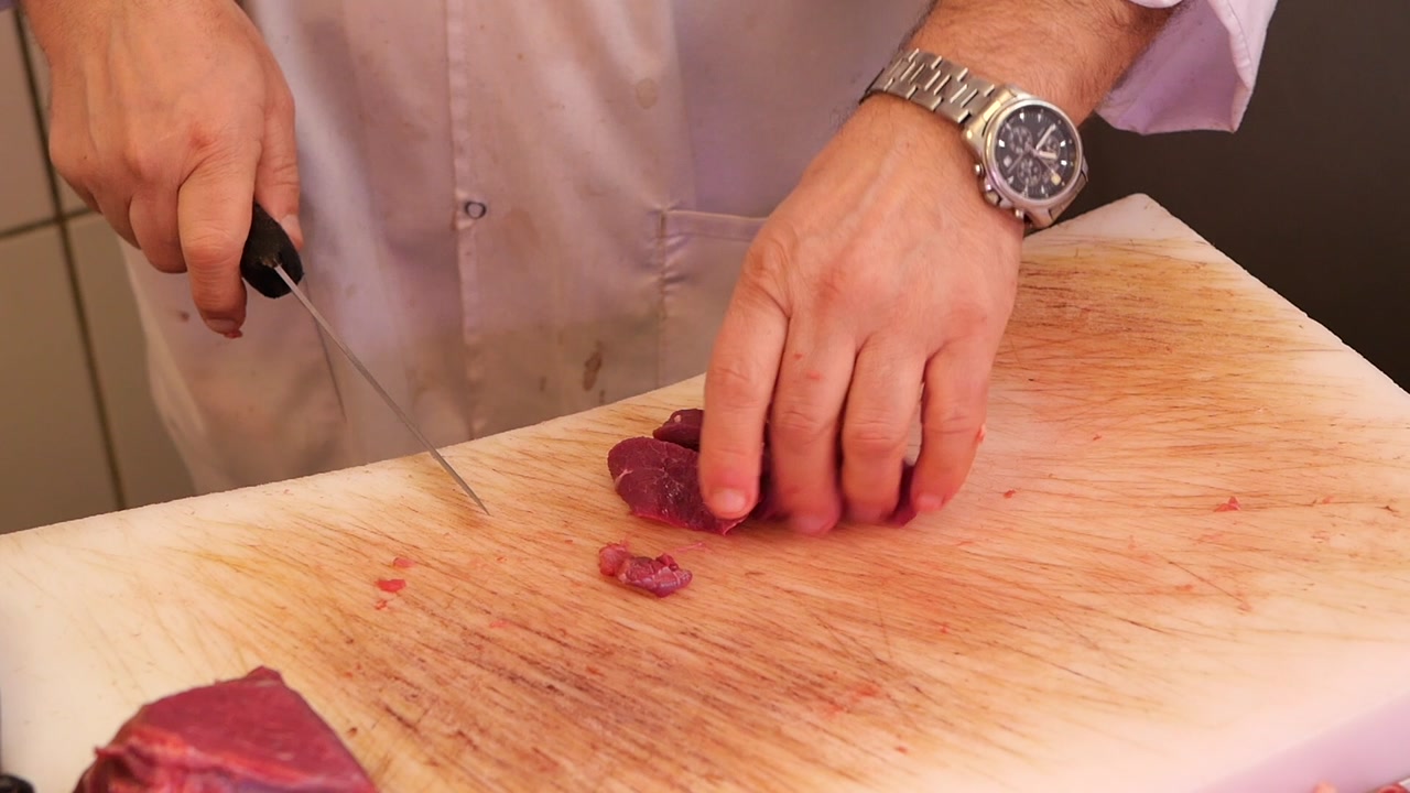 Close-up of a Butcher Slicing Raw Meat on a Cutting Board