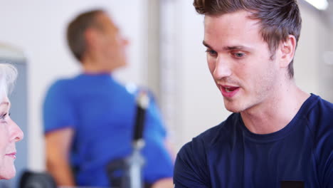 senior woman discussing exercise program with male personal trainer in gym