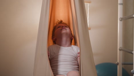 Curious-blond-boy-swaying-in-comfortable-beige-hammock