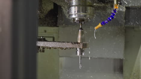 taladro cnc en movimiento, con pulverización de refrigerante y virutas metálicas en espiral en un taller de máquinas