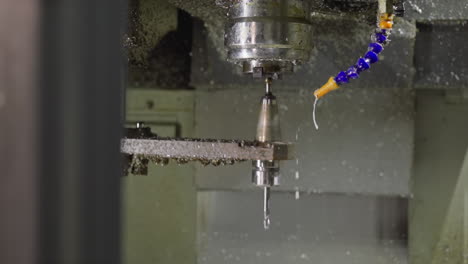 cnc drill in motion, with coolant spray and spiral metal shavings in a machine shop