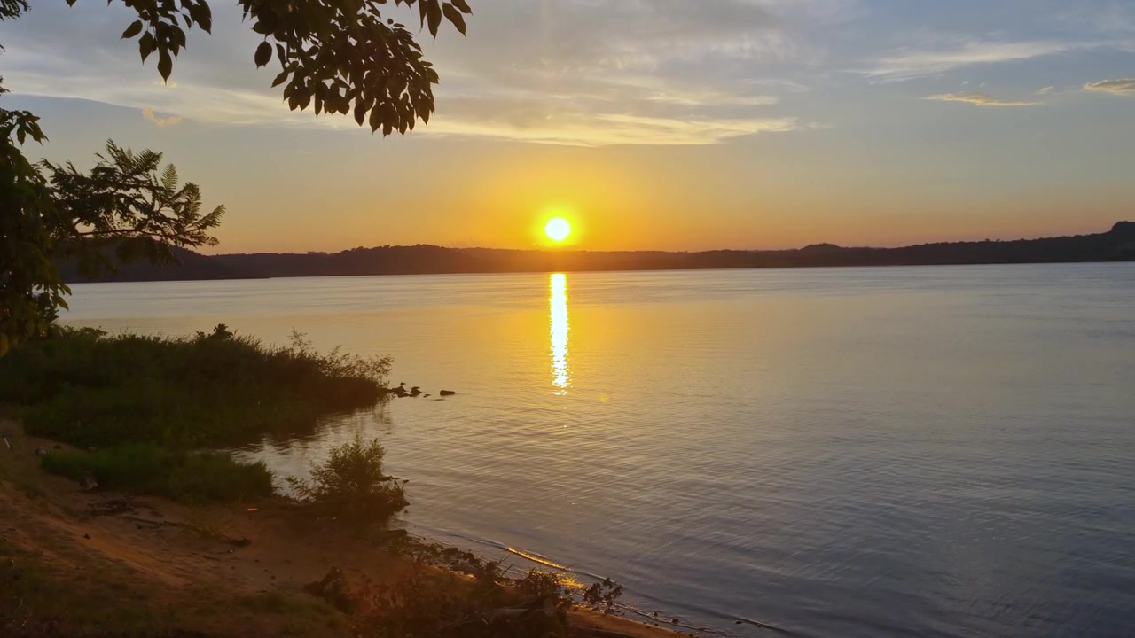 Tramonto sul Río Paraná vicino alla spiaggia Playa del Sol, San Ignacio, Argentina, con il Paraguay dall'altra parte del fiume calmo, paesaggio naturale tropicale e uno specchio d'acqua sereno.
