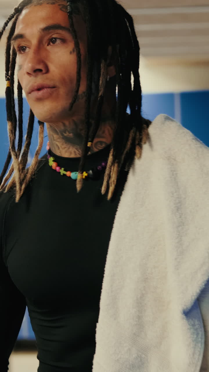 Uomo con dreadlock e tatuaggi in piedi in uno spogliatoio