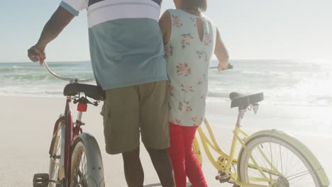 senior african american couple walking with bicycles on sunny beach