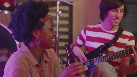 boy playing guitar while girl with beer bottle listening to him during a rehearsal in recording studio