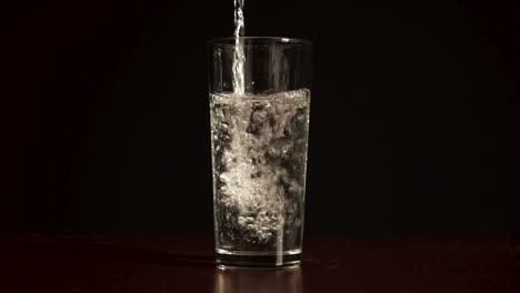 sirviendo agua en un vaso transparente, fondo negro, cámara lenta de luz natural