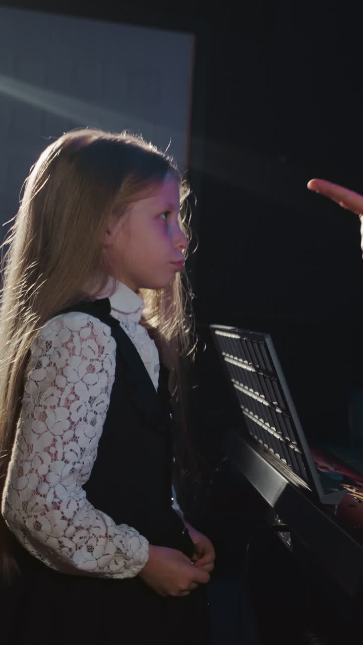 una estudiante colabora con un entrenador en un estudio de audio. un caballero toca el piano electrónico con una joven que hace ejercicios vocales. sesión de entrenamiento vocal