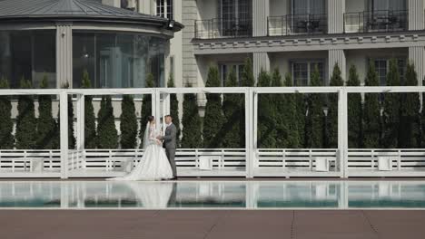 newlyweds caucasian bride groom walking near swimming pool, holding hands, wedding couple family