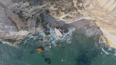 Aerial-view-of-water-with-waves-crashing-on-rocks-and-cliff-shot-in-4k-high-resolution