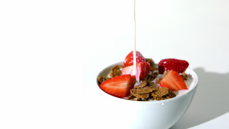 leche cayendo en un cuenco de cereales de trigo y fresas