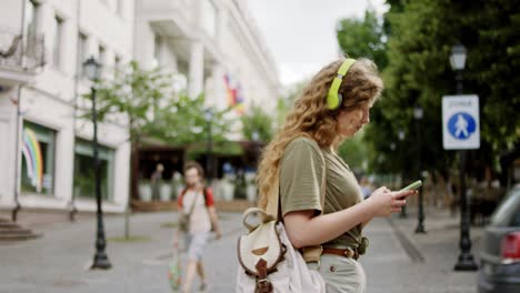 walking blonde hair lady down on the business street she holding her smartphone and wearing headphones concentrated typing something. shot on arri alexa mini