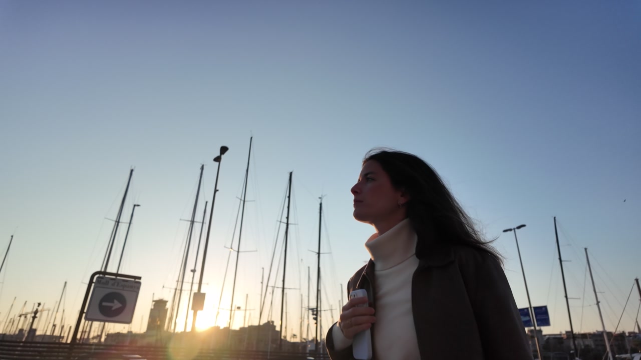 Woman walking by marina with sailboat masts sunset