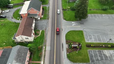 suburban american street with cars driving past quaint houses and a small parking lot. cloudy everyday life in a peaceful neighborhood, surrounded by greenery in spring. aerial birds eye shot. pa,usa