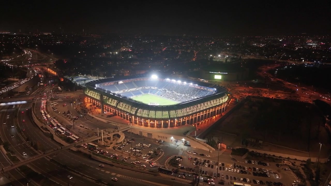 Jasno oświetlony kompleks Stadionu Teddy i otaczający ruch na autostradzie miejskiej nocą w Jerozolimie