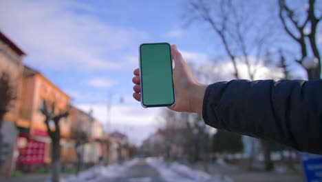 Hand man uses holding a mobile telephone with a vertical green screen background on of street houses people key smartphone technology touch message display