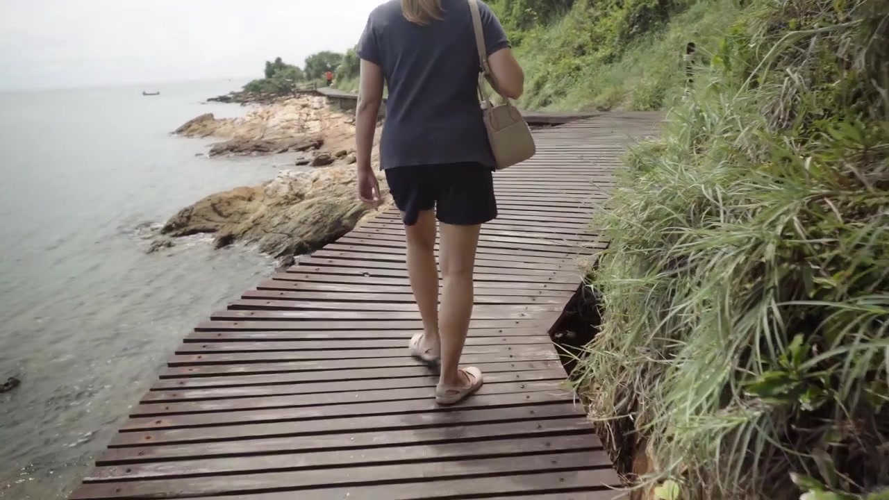 Carrellata dei passi di una donna che cammina con i sandali su una passerella costiera in legno nel Parco Nazionale di Khao Laem Ya Mu Ko Samet.