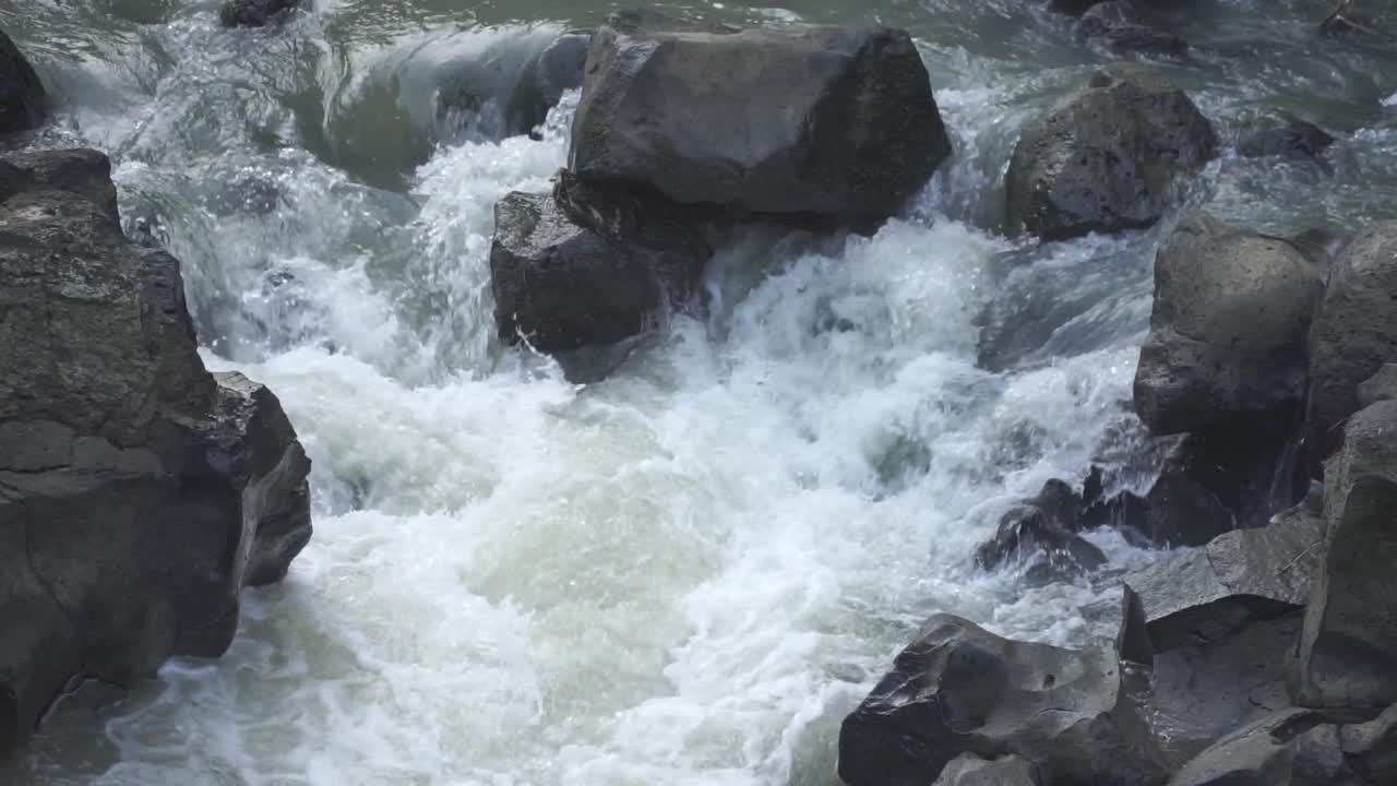 Close-up view of a powerful river current crashing against large rocks, creating intense white water and natural turbulence. Ideal for themes related to raw nature, force of water, and environmental.