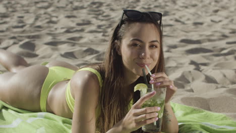 happy girl in bikini lying on beach and drinking cocktail