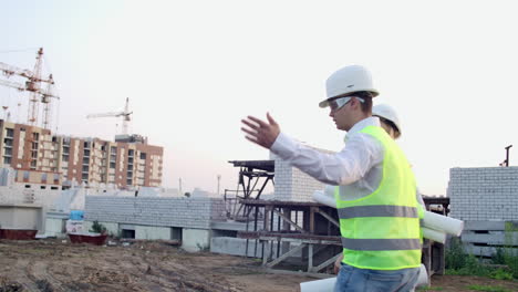 Ingenieur-Und-Techniker-Wenden-Sich-Auf-Der-Baustelle-Dem-Rücken-Zu,-Prüfen-Büropläne-Und-Technische-Zeichnungen-Und-Diskutieren.