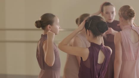 a group of young ballet students in black dancewear practicing positions in a spacious ballet studio with wooden flooring and wall-mounted barres. focused expressions and synchronized movements.