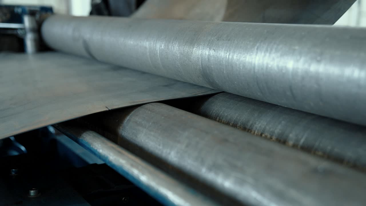 Sheet of metal is bent in a machine between two rotating rollers. Production of metal products at an industrial enterprise