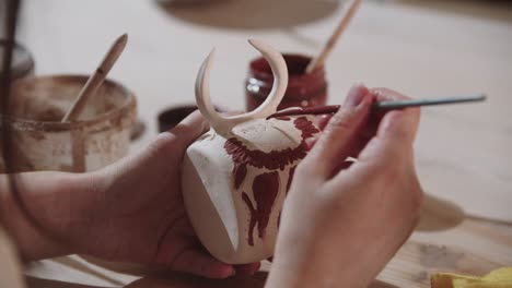 a woman potter painting on the ceramic cup with a brush