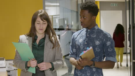 Female-And-Male-Colleagues-Walking-And-Talking-In-A-Corridor