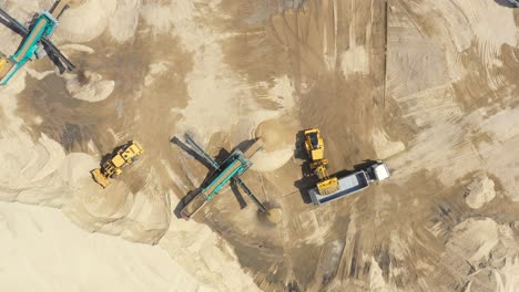 Aerial-view,-machinery-working-at-clay-quarry,-heavy-loaders,-large-trucks,-bulldozers,-excavators,-Sand-quarry,-Mining,-Truck-takes-raw-materials-from-the-quarry,-Large-clay-warehouse