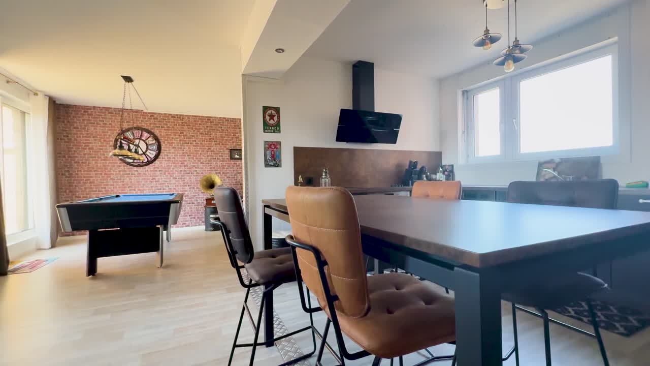 Wide-angle camera smoothly pans through a bright, retro-inspired apartment lounge featuring a billiard table, vintage decor, and modern kitchen under natural daylight