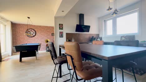 wide-angle camera smoothly pans through a bright, retro-inspired apartment lounge featuring a billiard table, vintage decor, and modern kitchen under natural daylight