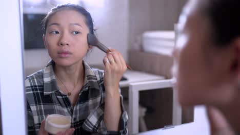 young woman applying makeup against mirror