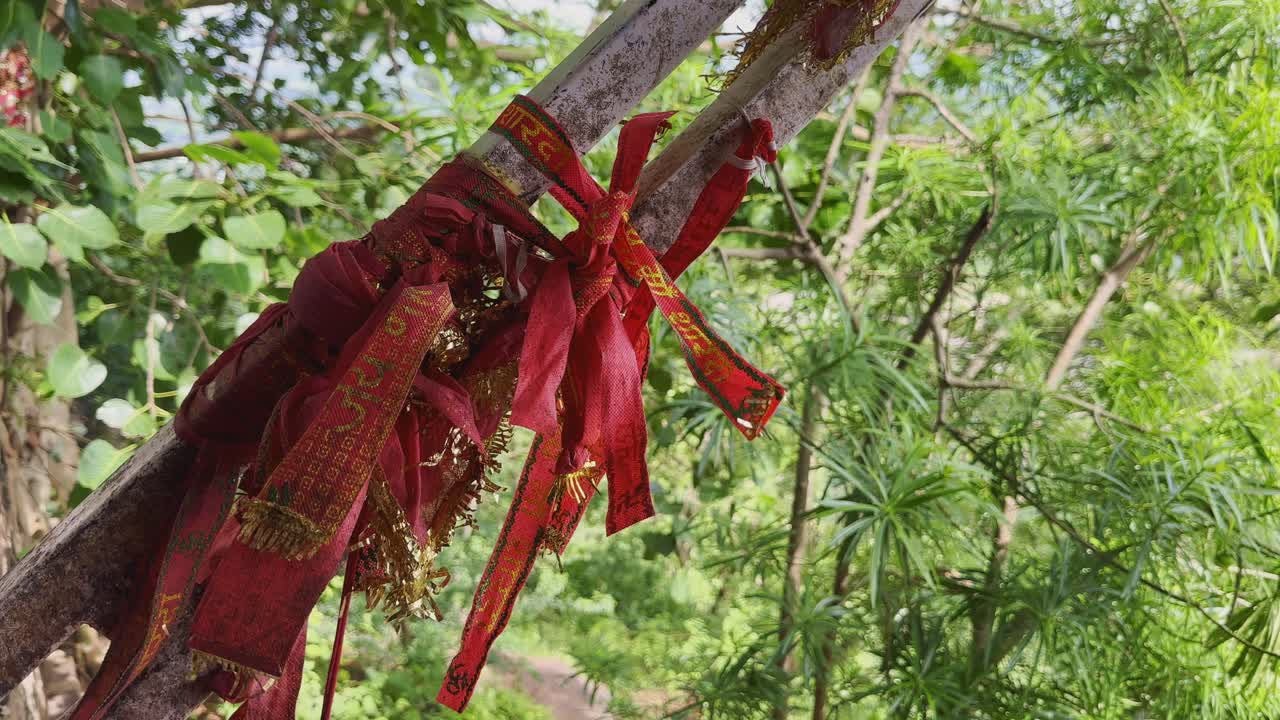 Foto close-up kain merah sakral yang diikatkan pada cabang pohon di Kuil Maihar Sharda Devi, Madhya Pradesh. Para pemuja mengikat kain ini sambil berdoa agar permohonan mereka dikabulkan di Shakti Peeth yang dihormati ini