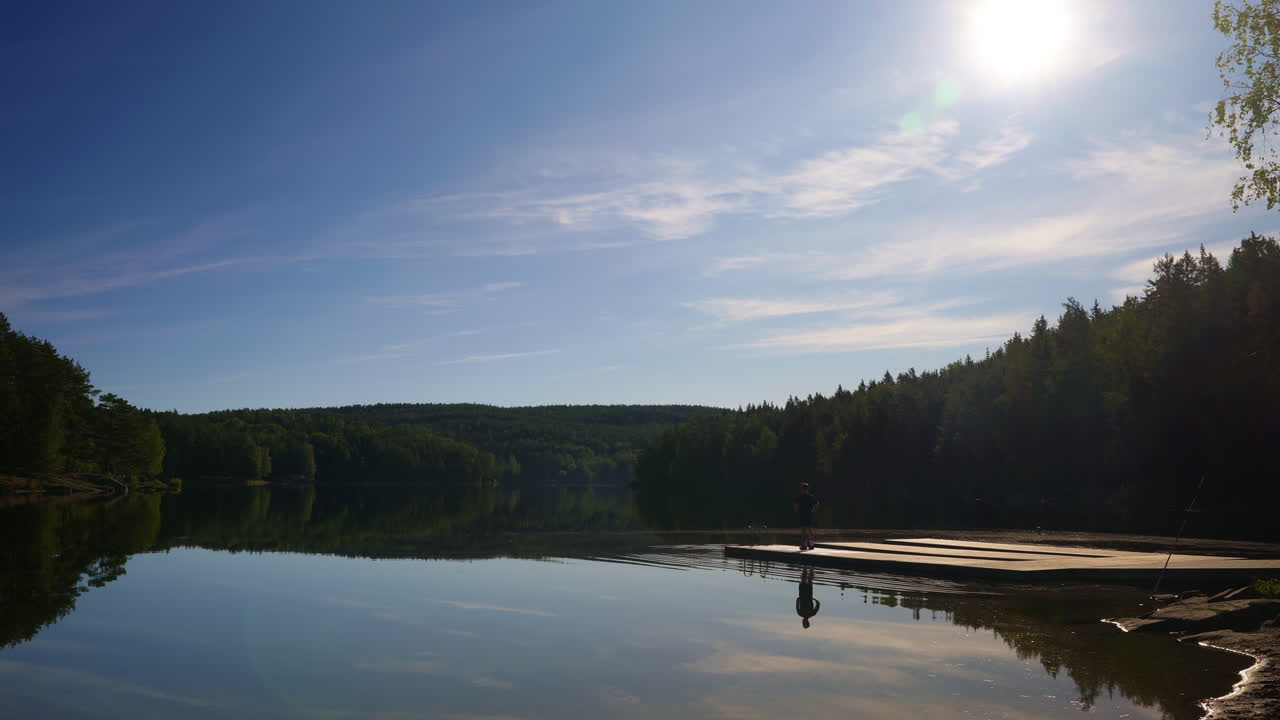 Man jogs onto a pier in the lake on a sunny day with very calm water and almost no clouds in the sky